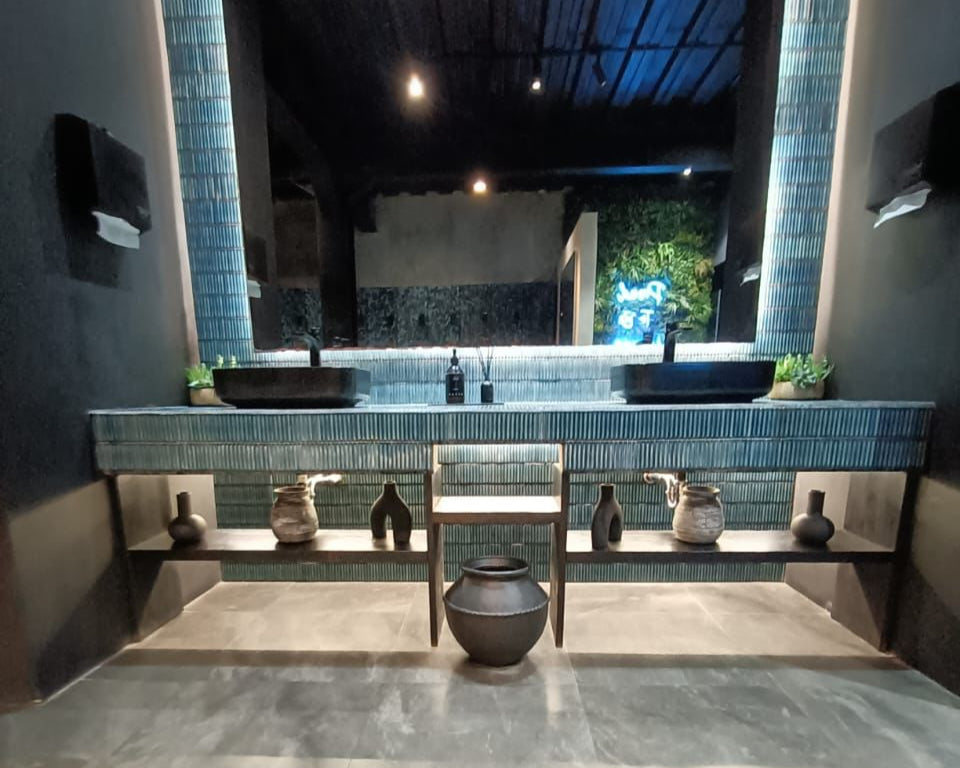 Modern washroom interior at Wrong Gym Bali featuring dual black basins, decorative vases, soft lighting, and a tiled mirror wall with a subtle neon glow in the background.