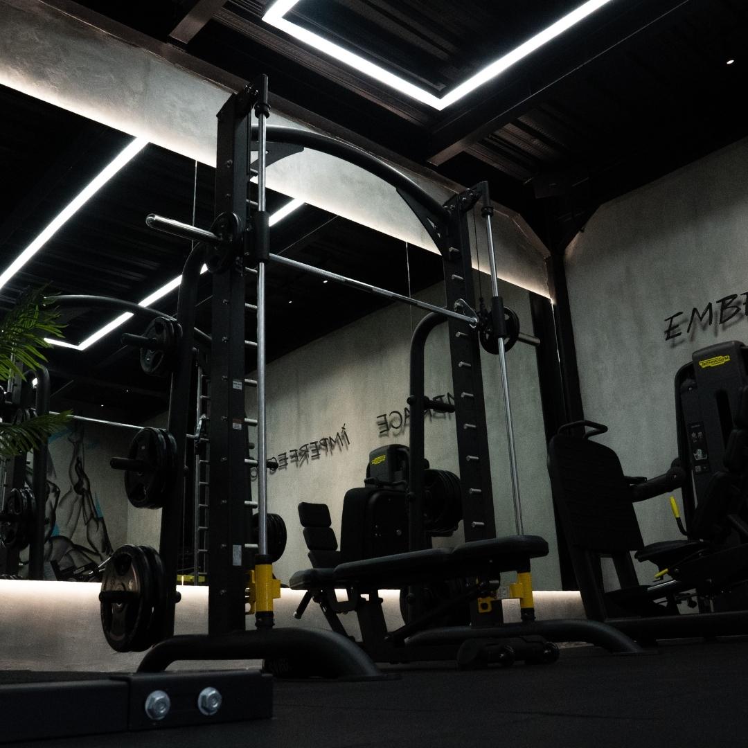 Strength training equipment in the dimly lit Booty Room at Wrong Gym Bali, featuring neon ceiling lights and mirrored walls.