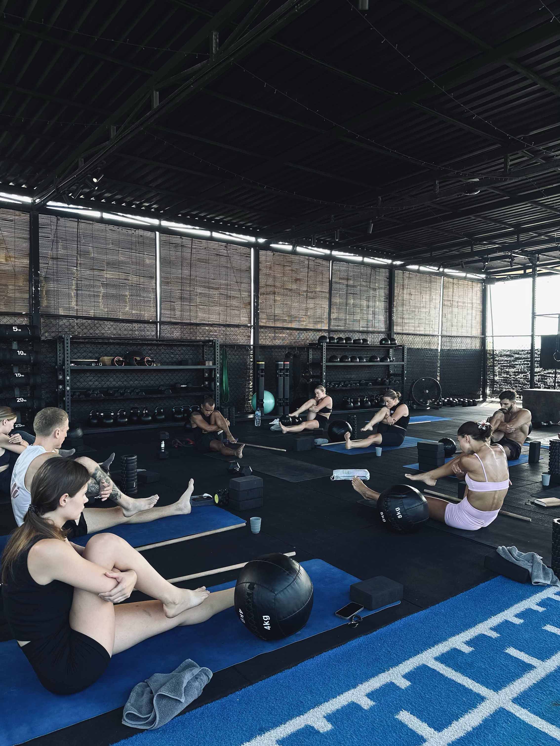 Participants in a flexibility training class at Wrong Gym Bali using mats, medicine balls, and mobility tools in a covered open-air studio.