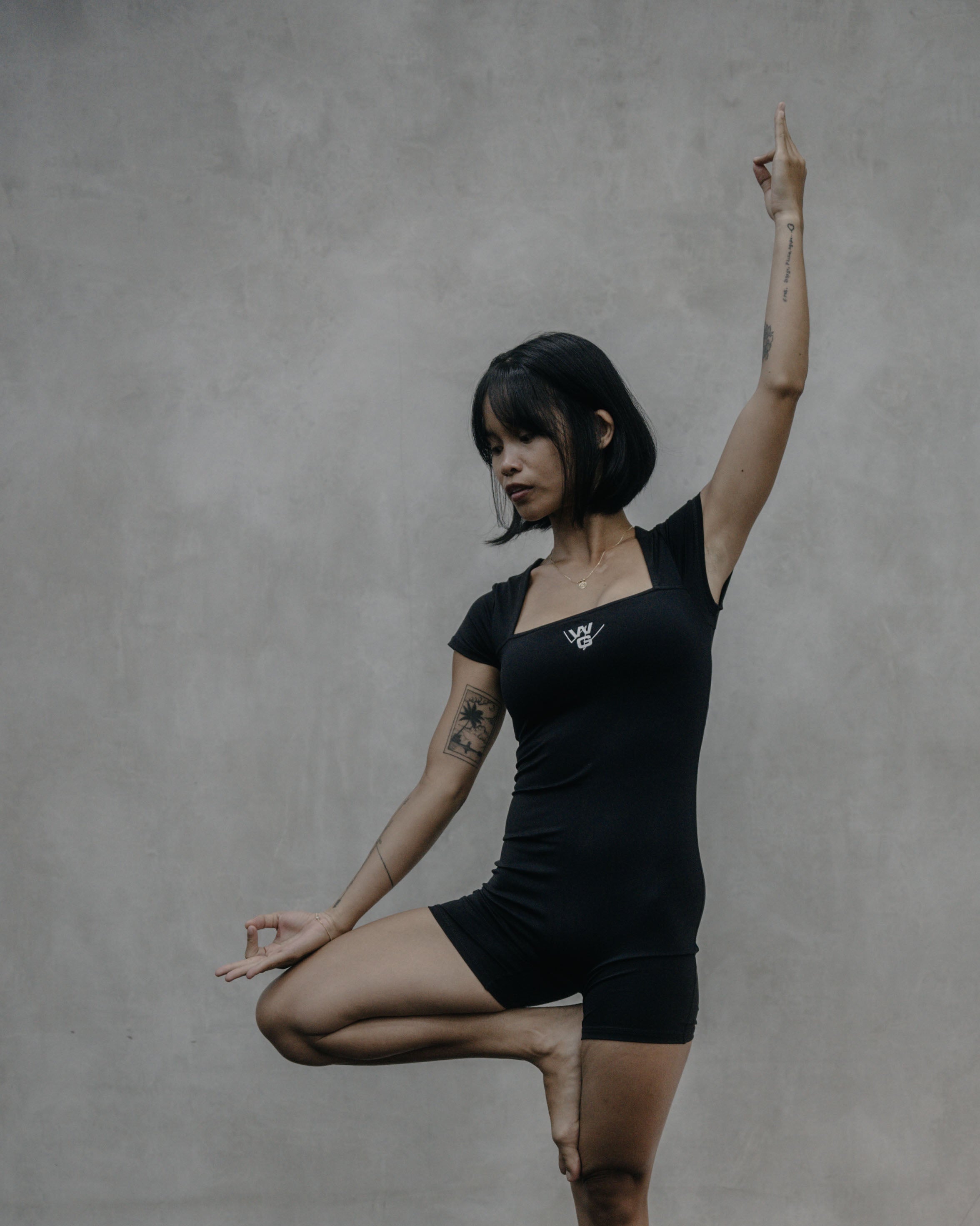 Yin Yoga instructor at Wrong Gym Bali holding tree pose indoors, wearing black activewear with WG logo.