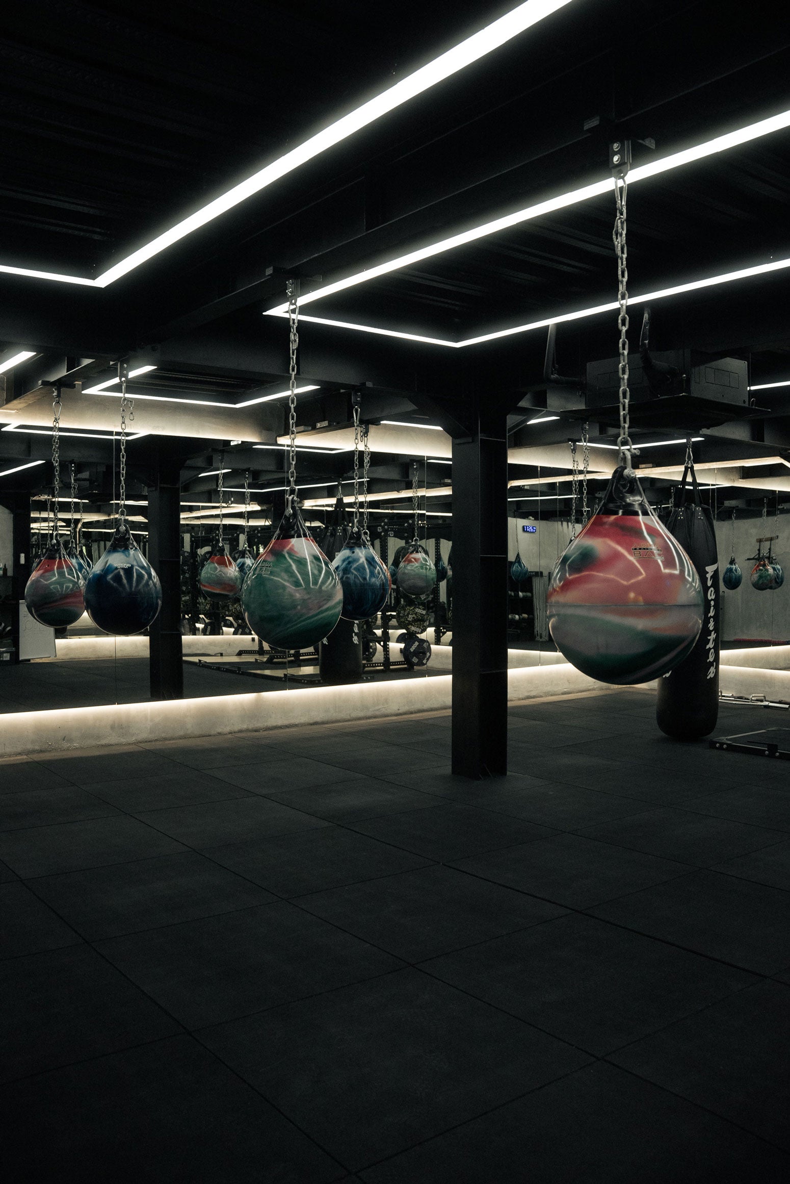 Boxing bags hanging in Wrong Gym Bali's Hell Room under neon strip lighting.