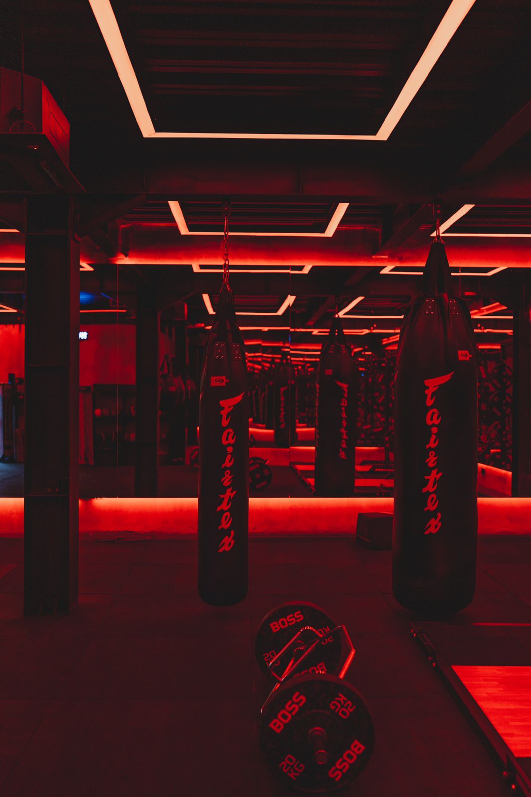 Red-lit boxing room at Wrong Gym Bali with hanging Fairtex punching bags and barbell weights on the floor.