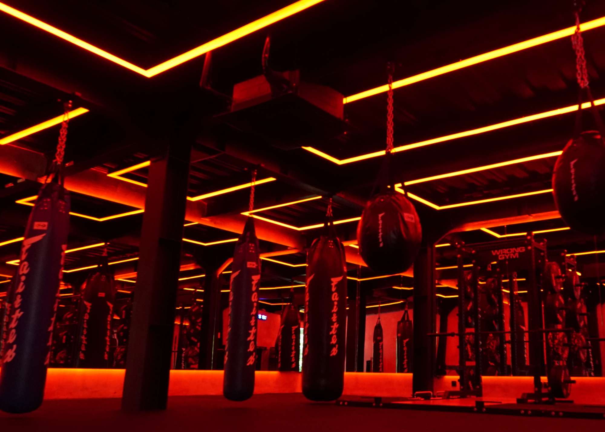Intense red-lit boxing room at Wrong Gym Bali, featuring rows of Fairtex heavy bags suspended from the ceiling with mirrored walls reflecting the vibrant lighting grid.