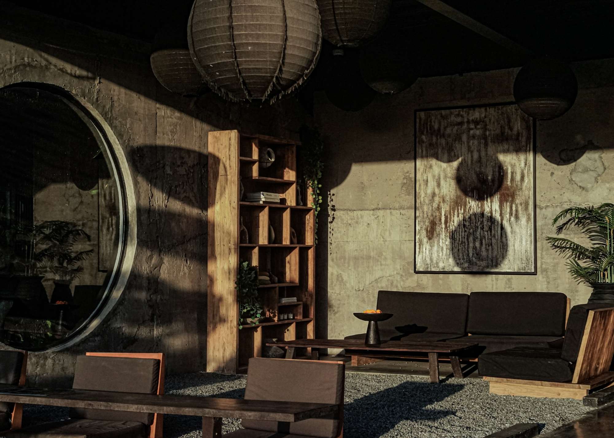 Earth-toned lounge space at Wrong Gym Bali, featuring textured concrete walls, a circular window, wooden furniture, abstract art, and warm afternoon light.