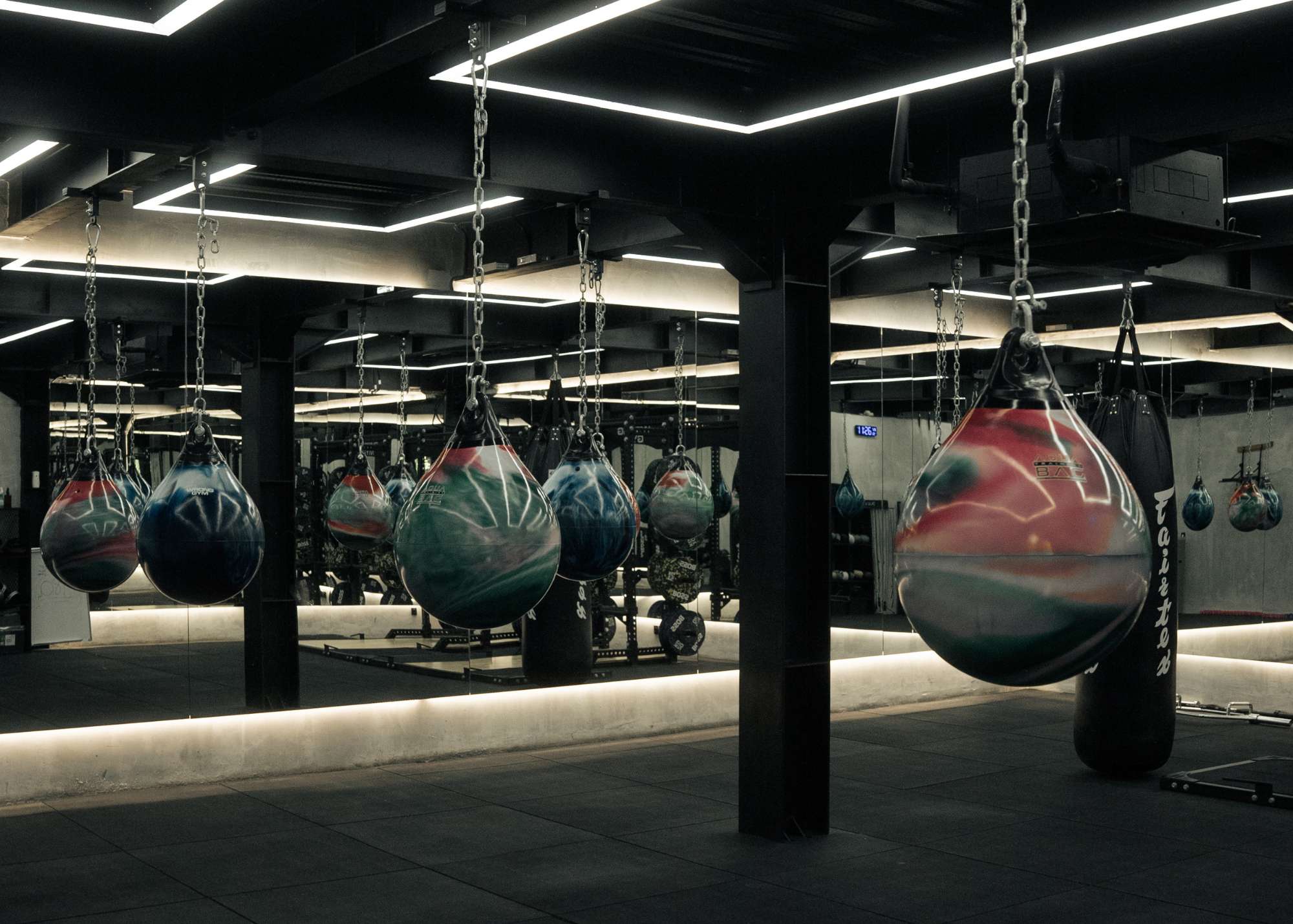 Boxing area at Wrong Gym Bali featuring a row of colourful water-filled punching bags suspended from the ceiling, mirrored walls reflecting the modern industrial interior.