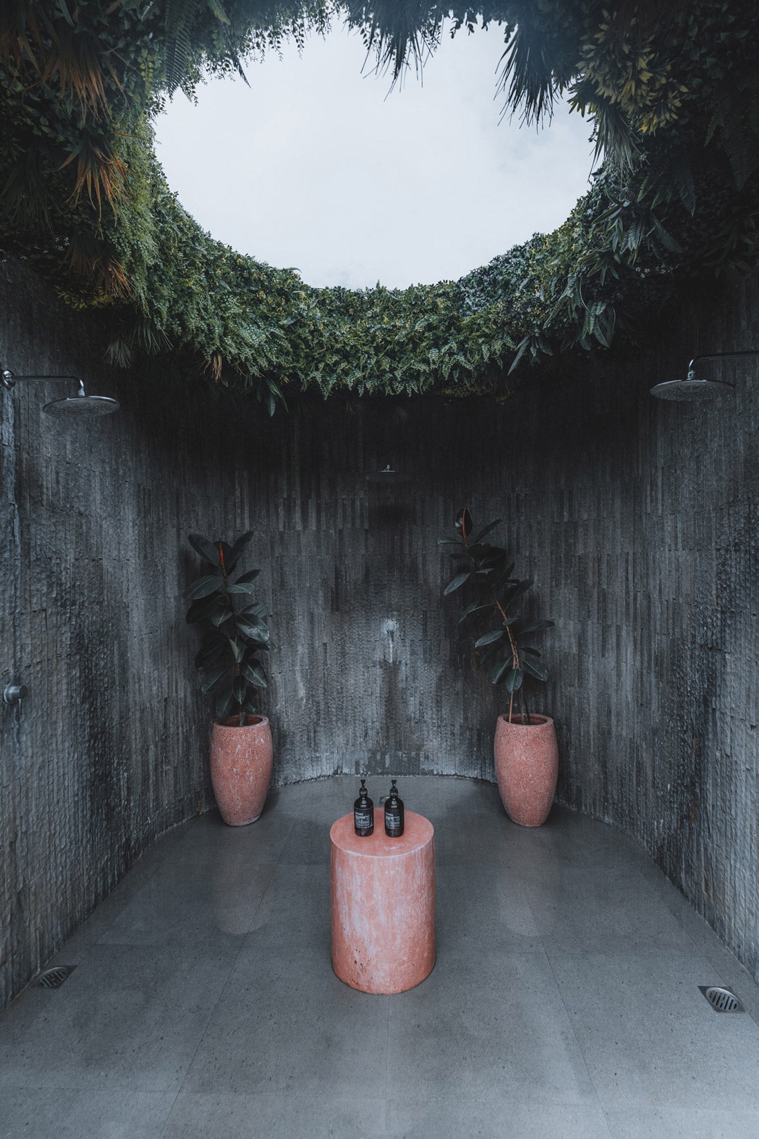 Outdoor circular stone shower at Wrong Gym Bali with skylight, greenery, and potted plants.