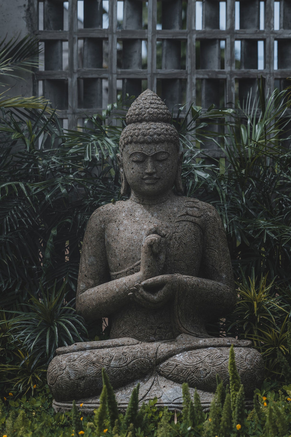 Stone Buddha statue in a meditative pose, surrounded by lush greenery at Wrong Gym Bali.