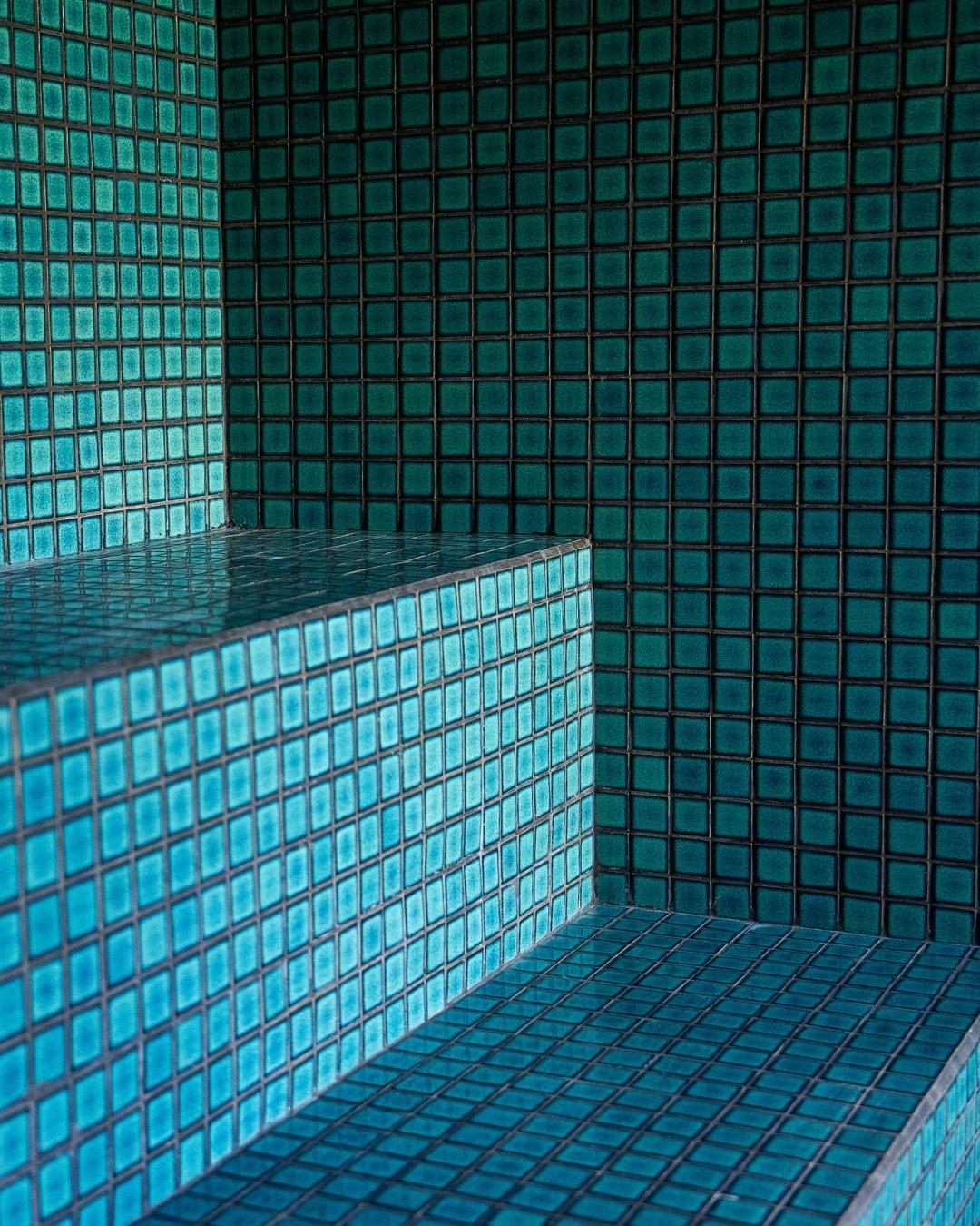 Close-up view of blue and teal mosaic tiles in the steam room at Wrong Gym Bali’s recovery area, featuring geometric seating design and tranquil spa ambiance.