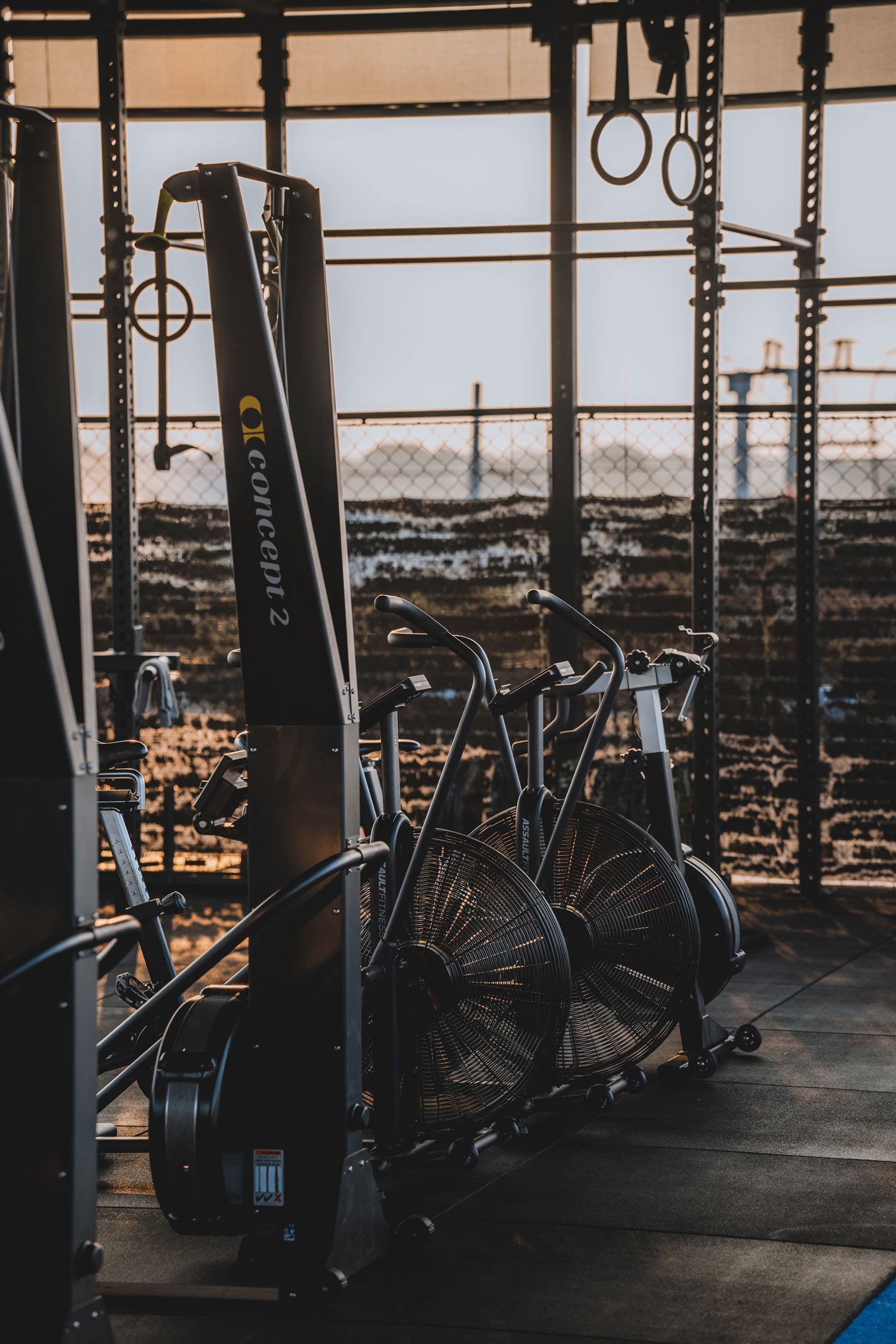 Concept2 ski erg and assault bikes on the rooftop gym area at Wrong Gym Bali, lit by warm natural light.