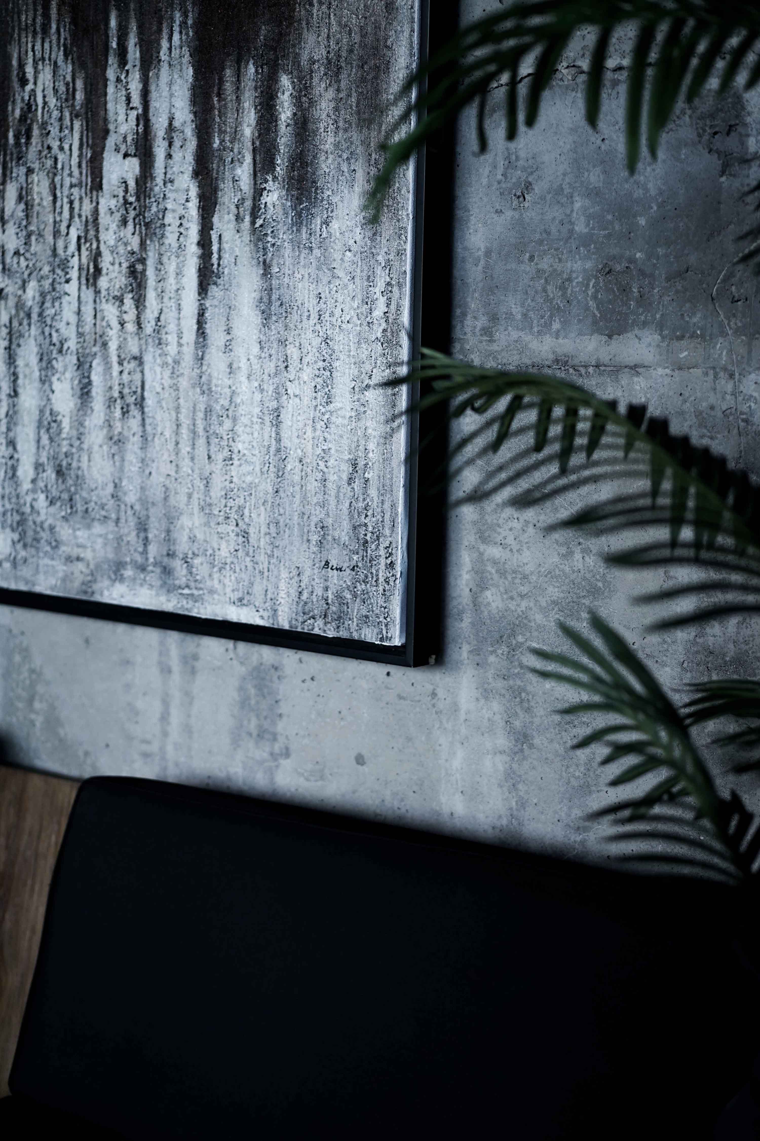 Abstract black-and-white painting on a concrete wall with indoor palm leaves at Wrong Gym Bali spa lounge.
