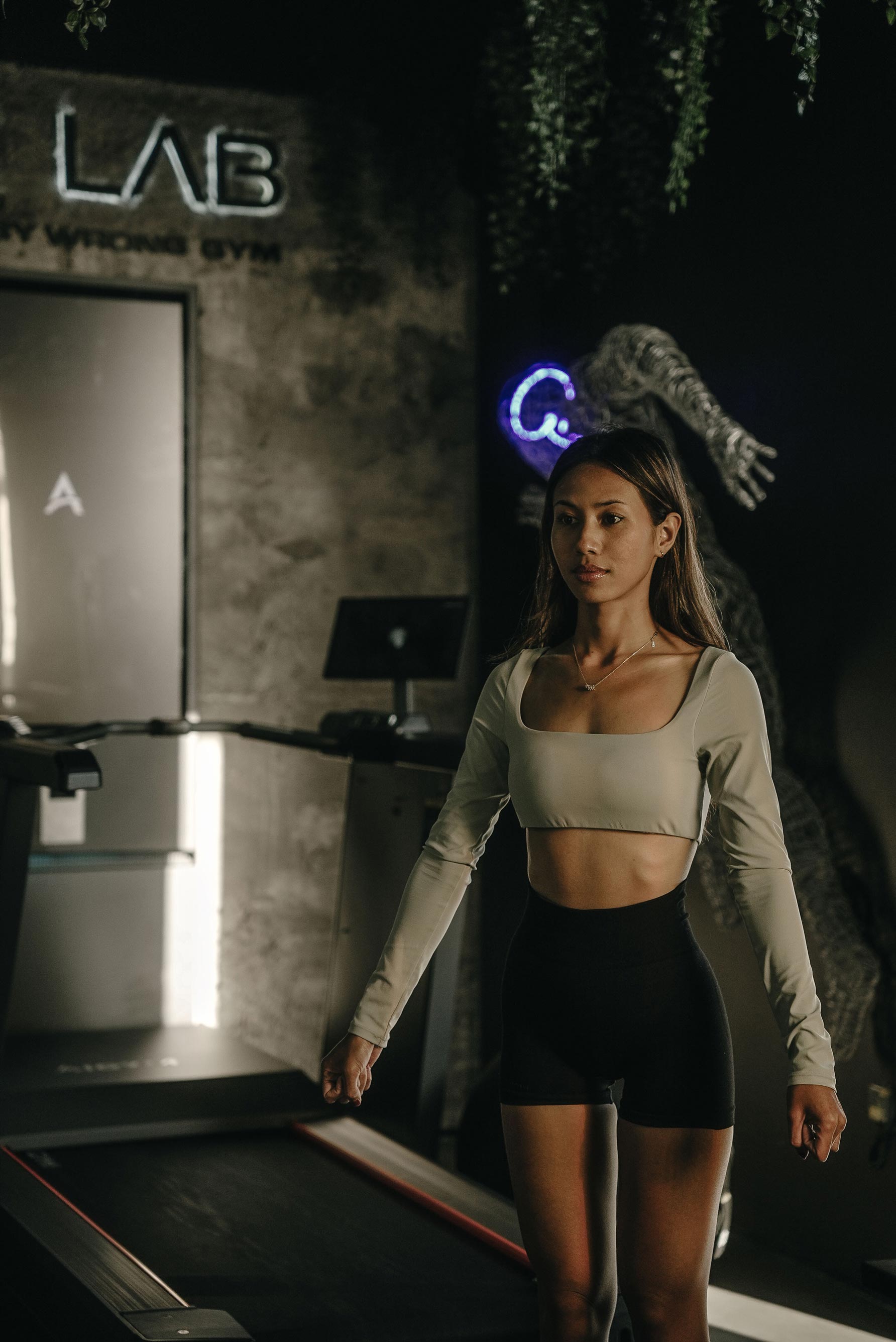 Female athlete walking on a treadmill inside The Lab at Wrong Gym Bali, with neon-lit wireframe art and modern training equipment in the background.