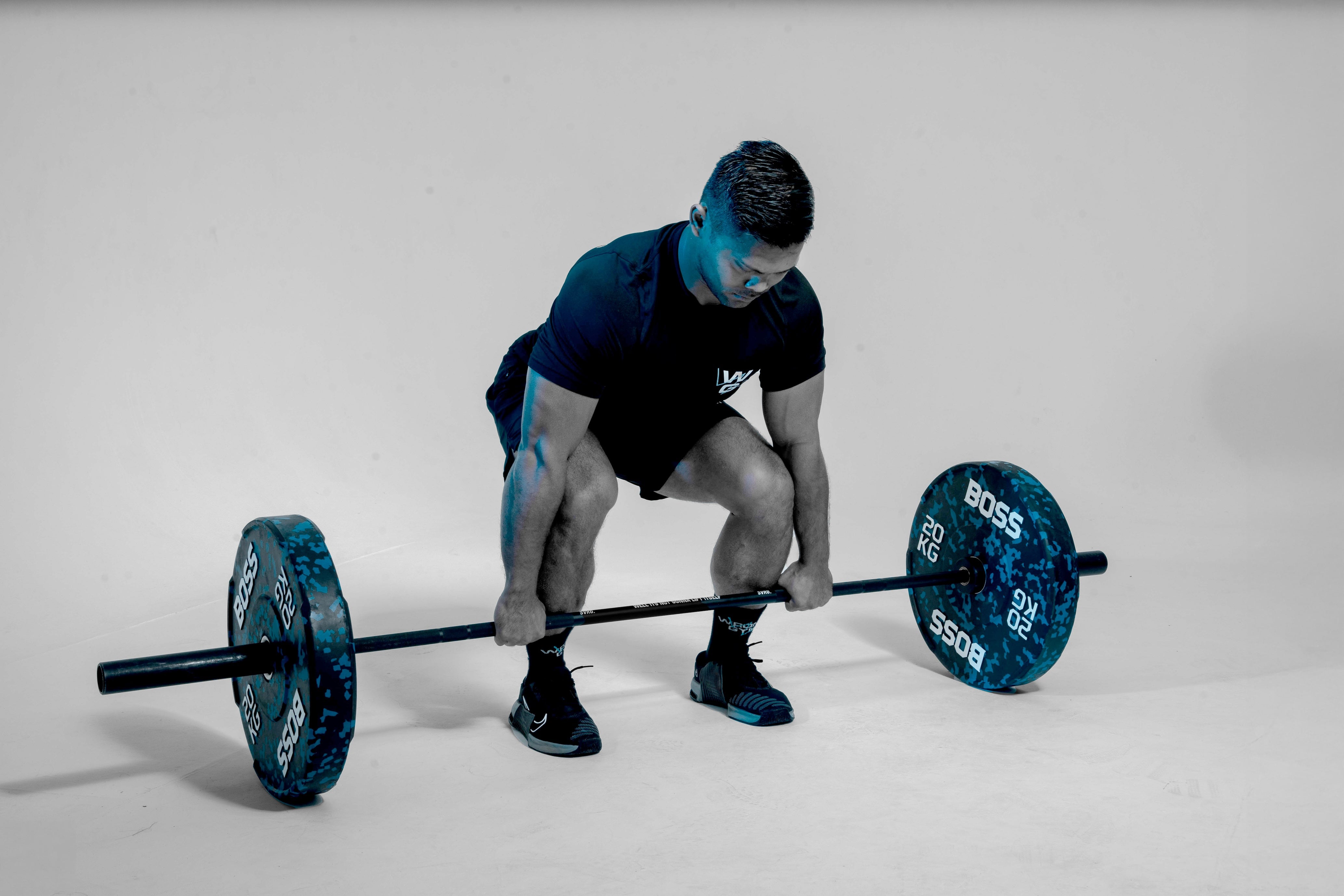 Prima, a trainer at Wrong Gym Bali, performing a deadlift with 20kg BOSS weight plates in a studio setting.