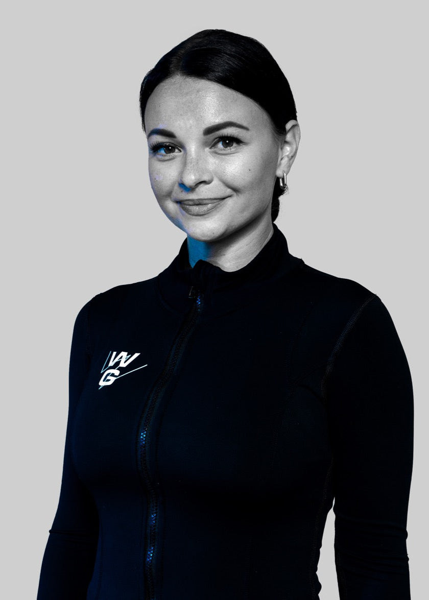 Polina, trainer at Wrong Gym Bali, smiling confidently in a WG-branded zip-up top against a grey background.