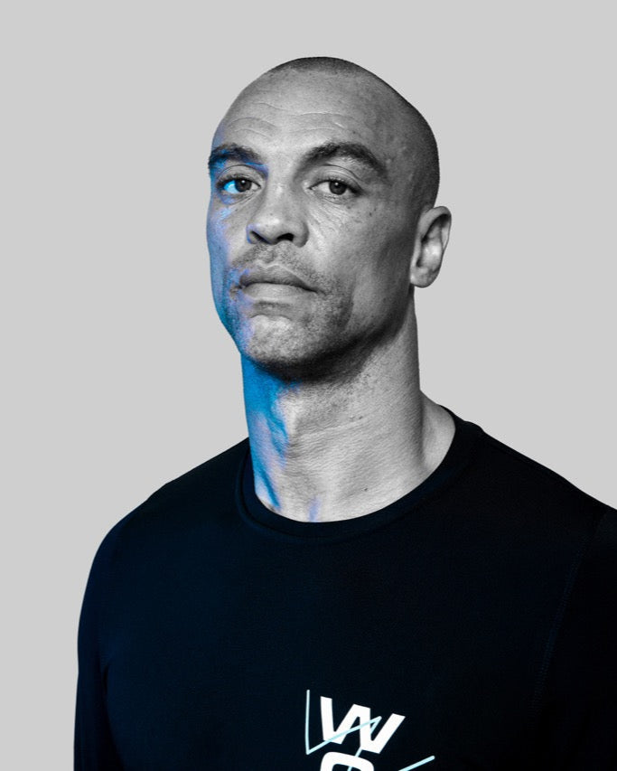 Simon, trainer at Wrong Gym Bali, in a black WG-branded shirt, posing confidently against a grey background.
