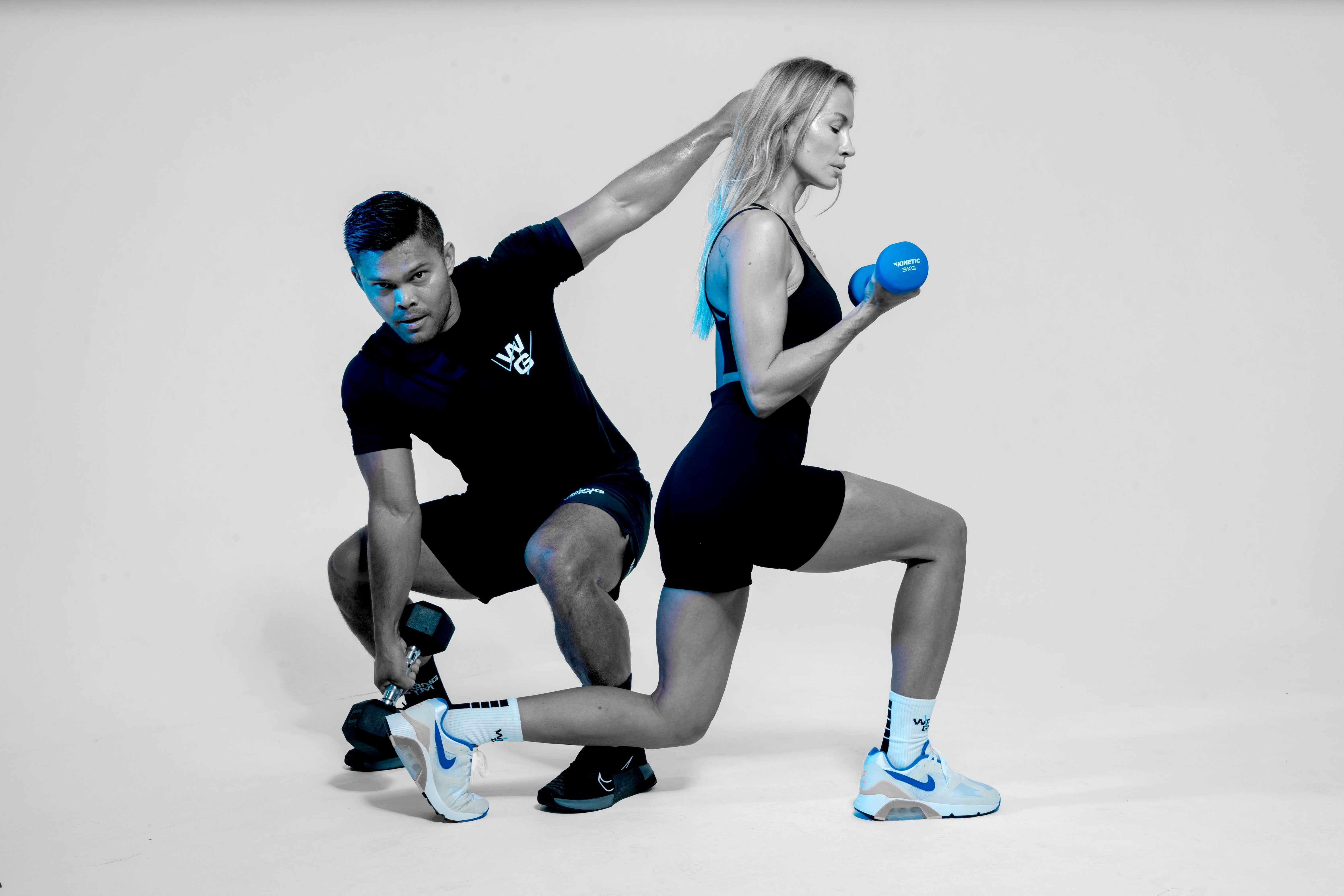 Male and female trainers from Wrong Gym Bali performing a lunge and curl exercise together, showcasing functional strength training.