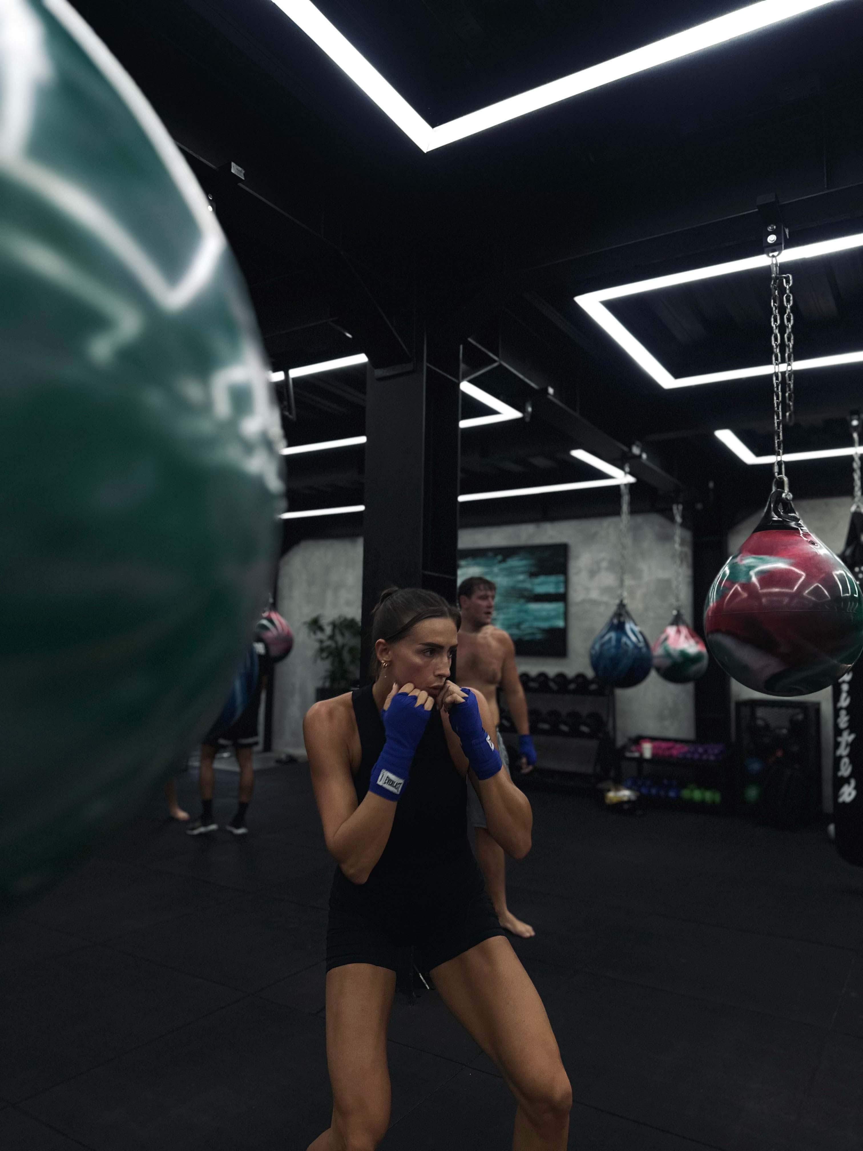 Female participant practicing boxing fundamentals with hand wraps and focus bags at Wrong Gym Bali's indoor training space.