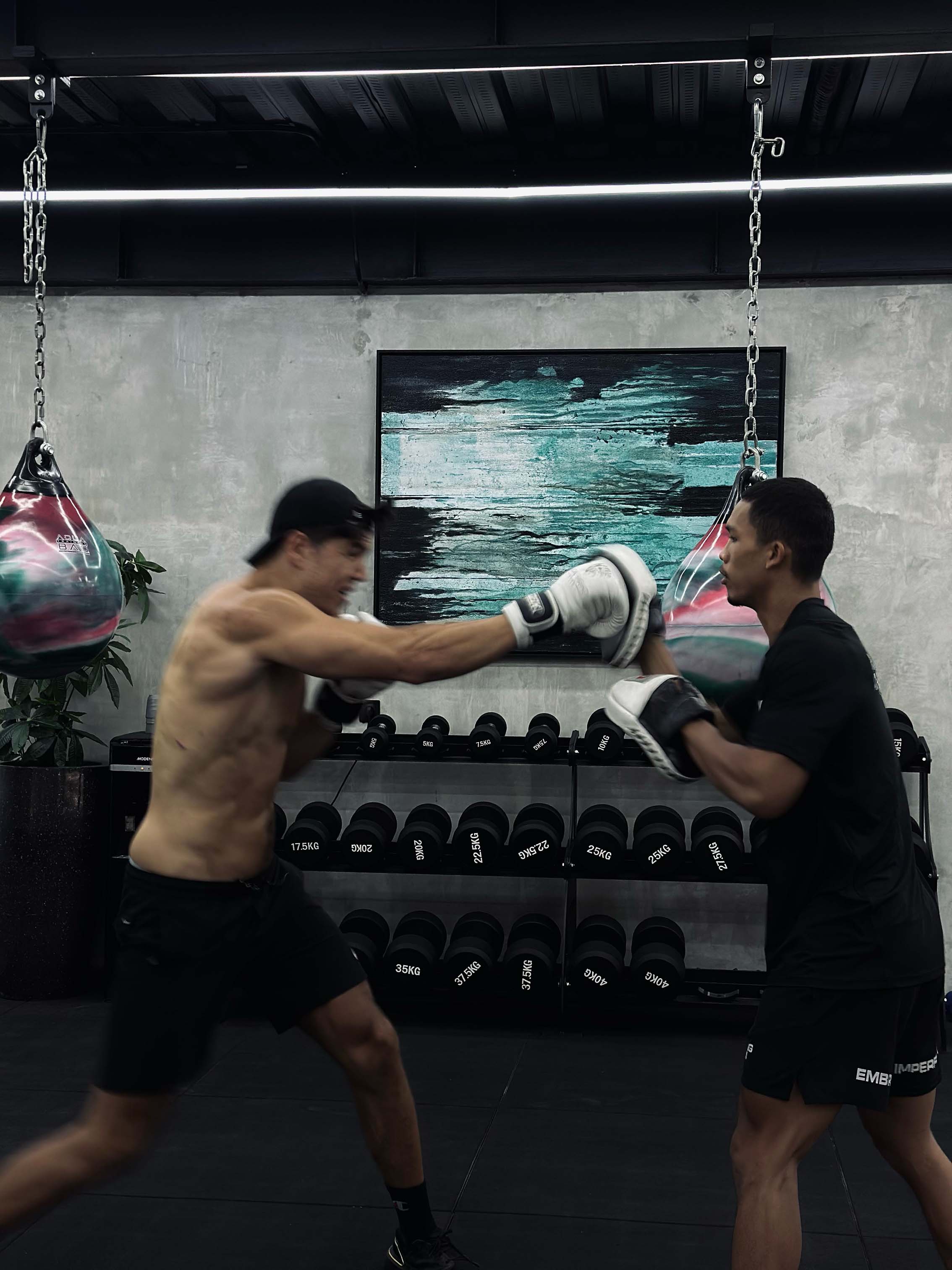 Two male athletes practicing high-intensity boxing combinations with gloves and pads at Wrong Gym Bali's Fit Combat class, surrounded by gym equipment.