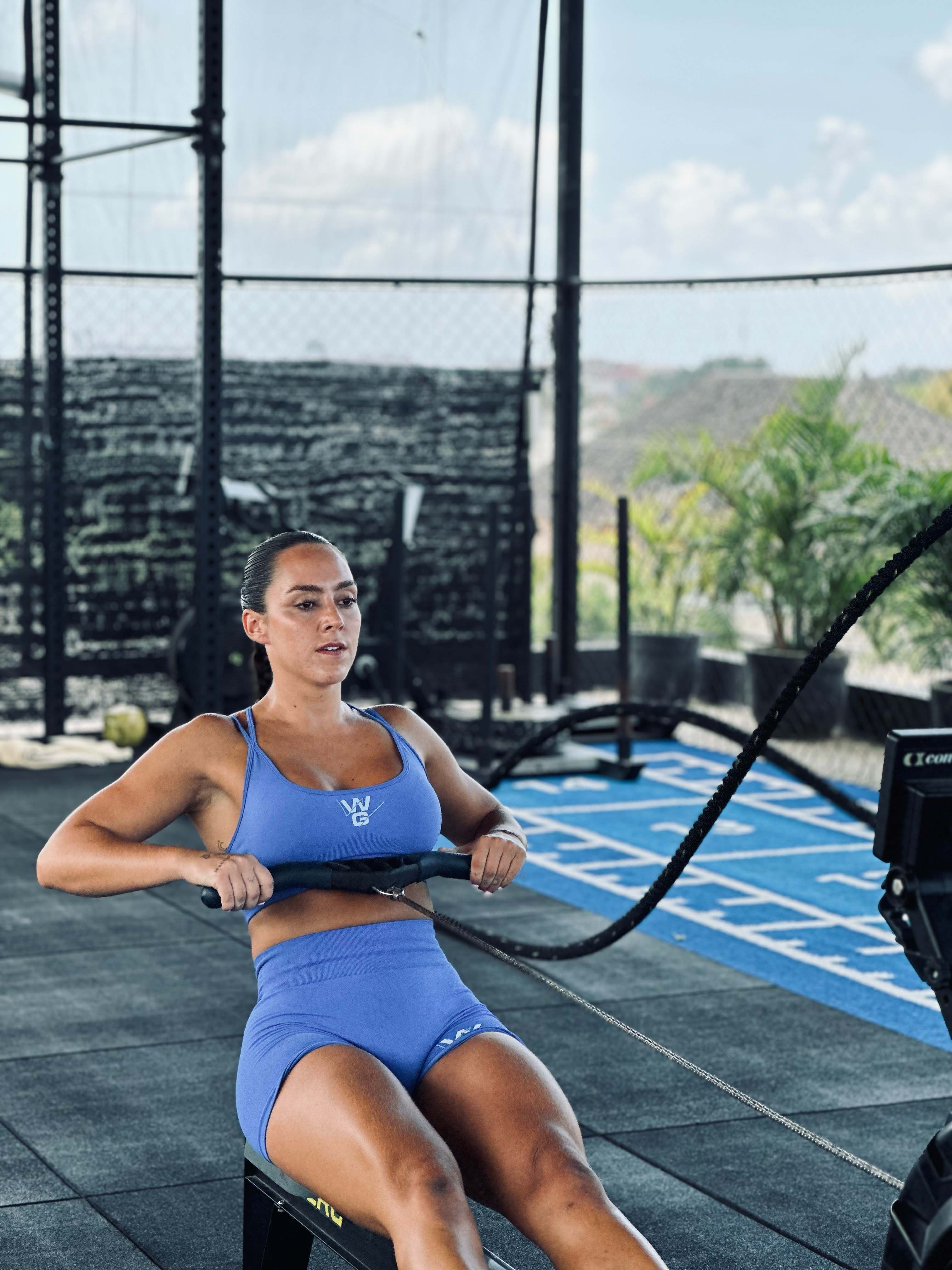 Female athlete in blue activewear using a Concept2 rowing machine during a high-intensity HIIT Classic class at Wrong Gym Bali