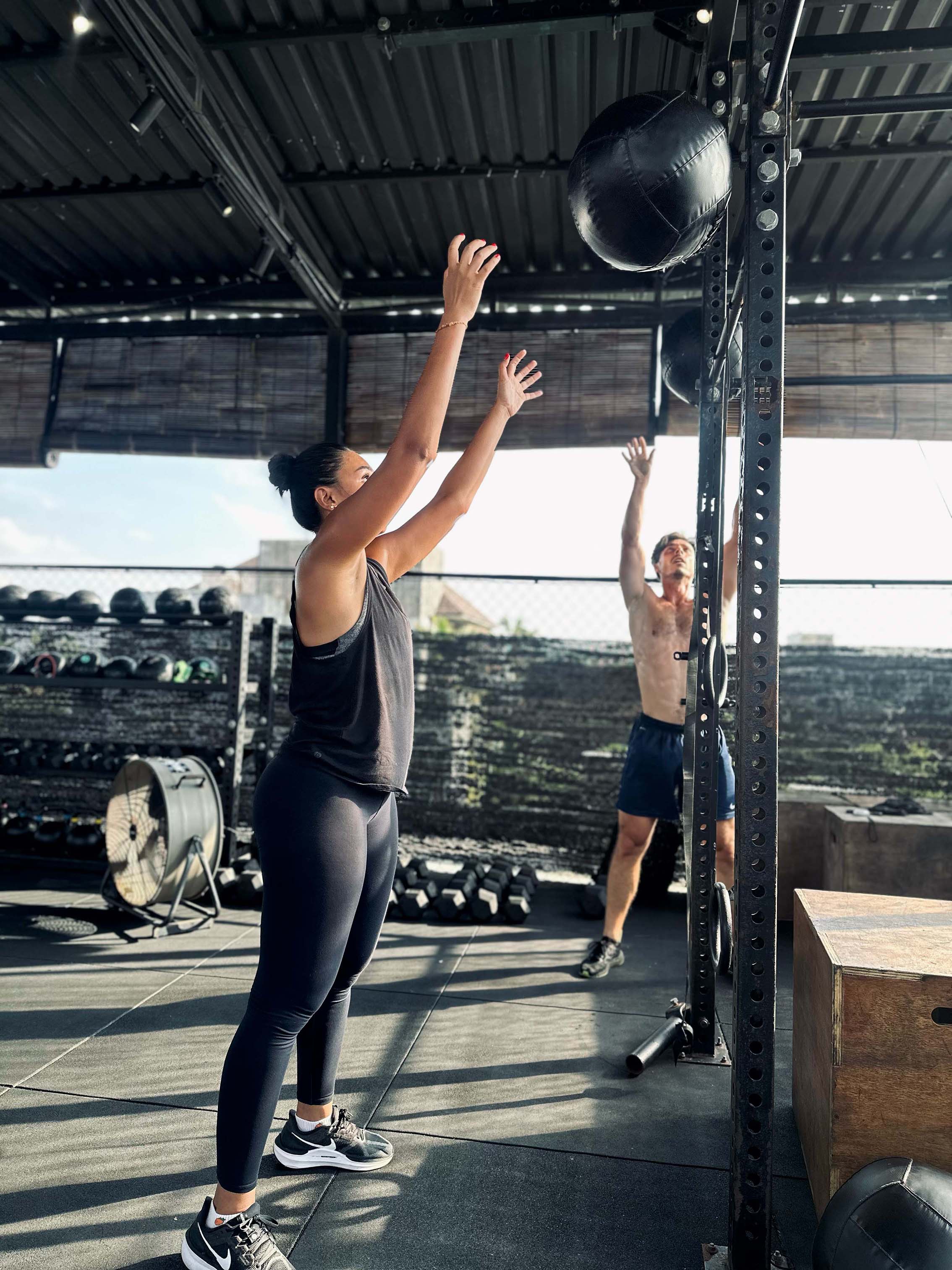 Man and woman performing wall ball throws during a Sculpt & Sweat HIIT class at Wrong Gym Bali, surrounded by functional fitness equipment.