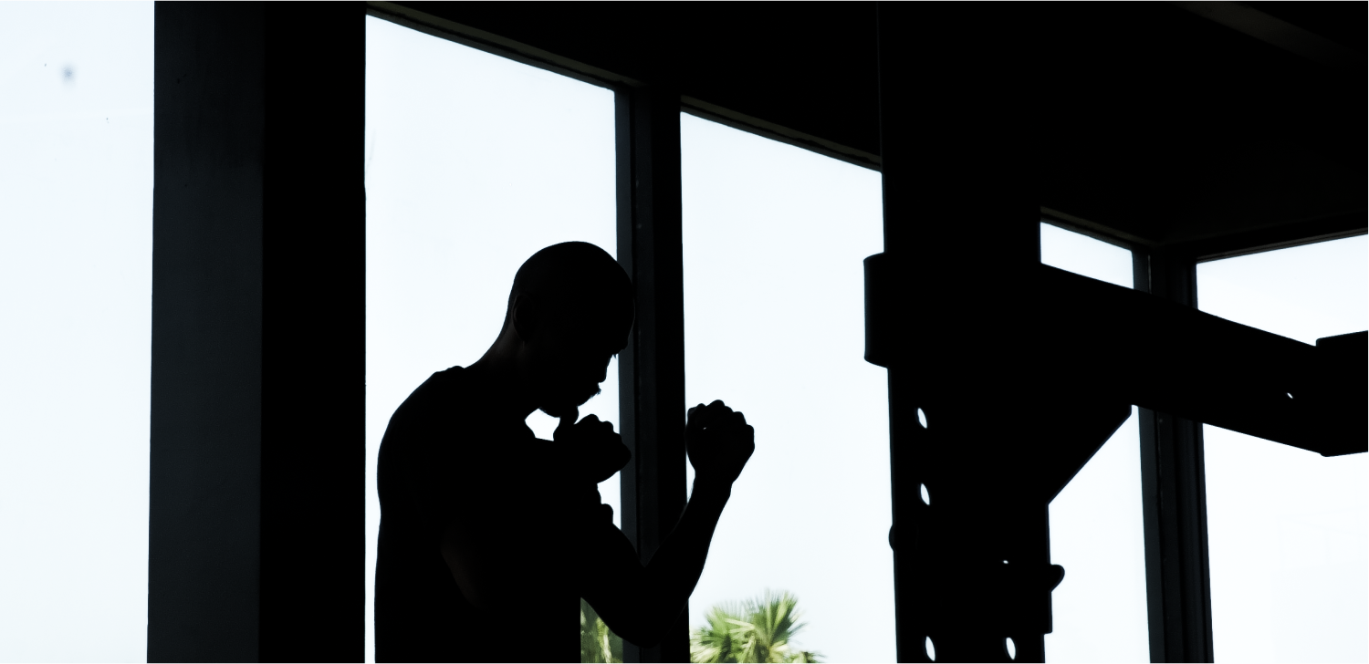 Silhouette of a person in a boxing stance inside a gym, with large windows in the background.