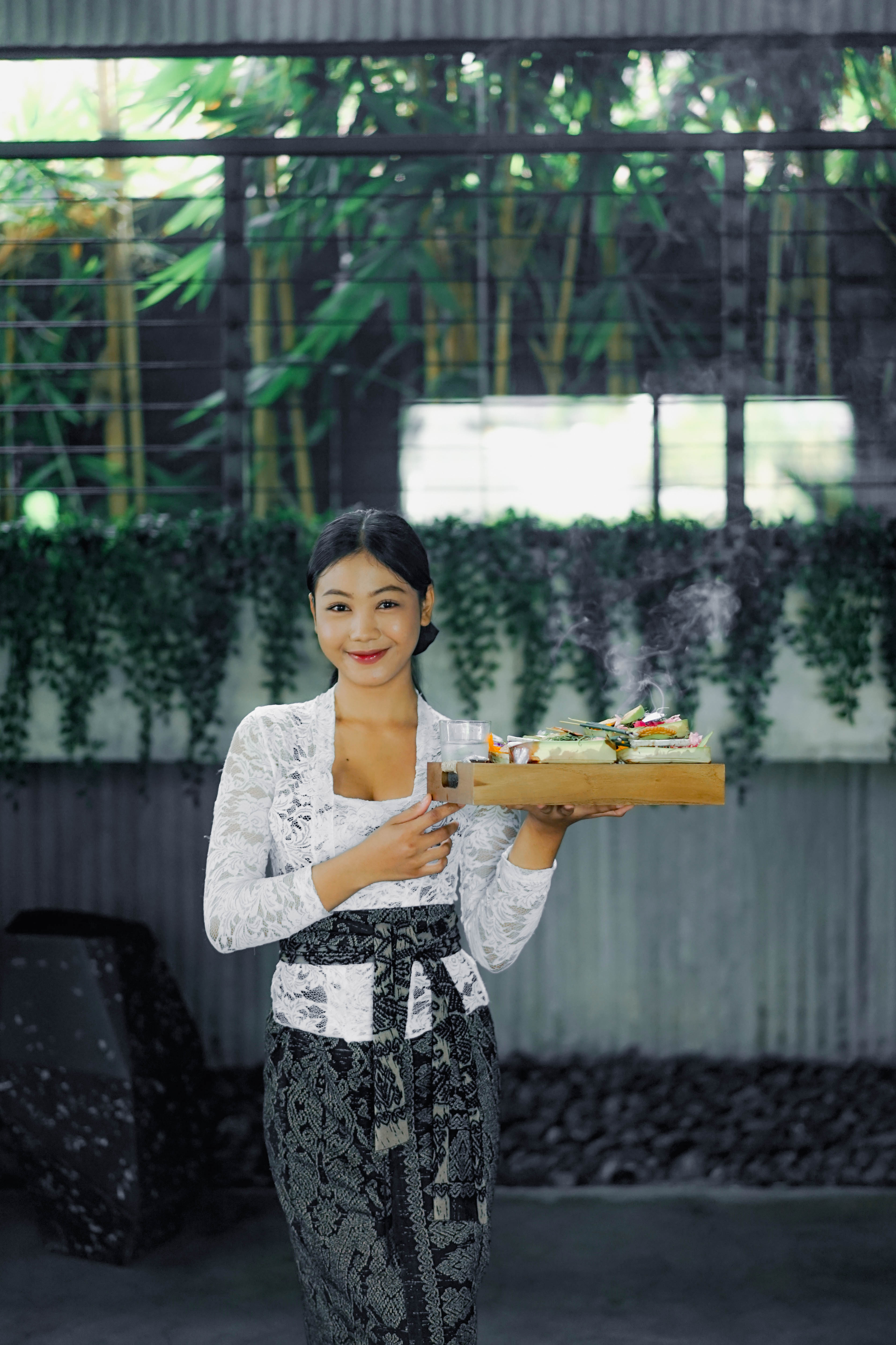 Smiling woman in traditional Balinese ceremonial attire holding a wooden tray with offerings at Wrong Gym Bali.