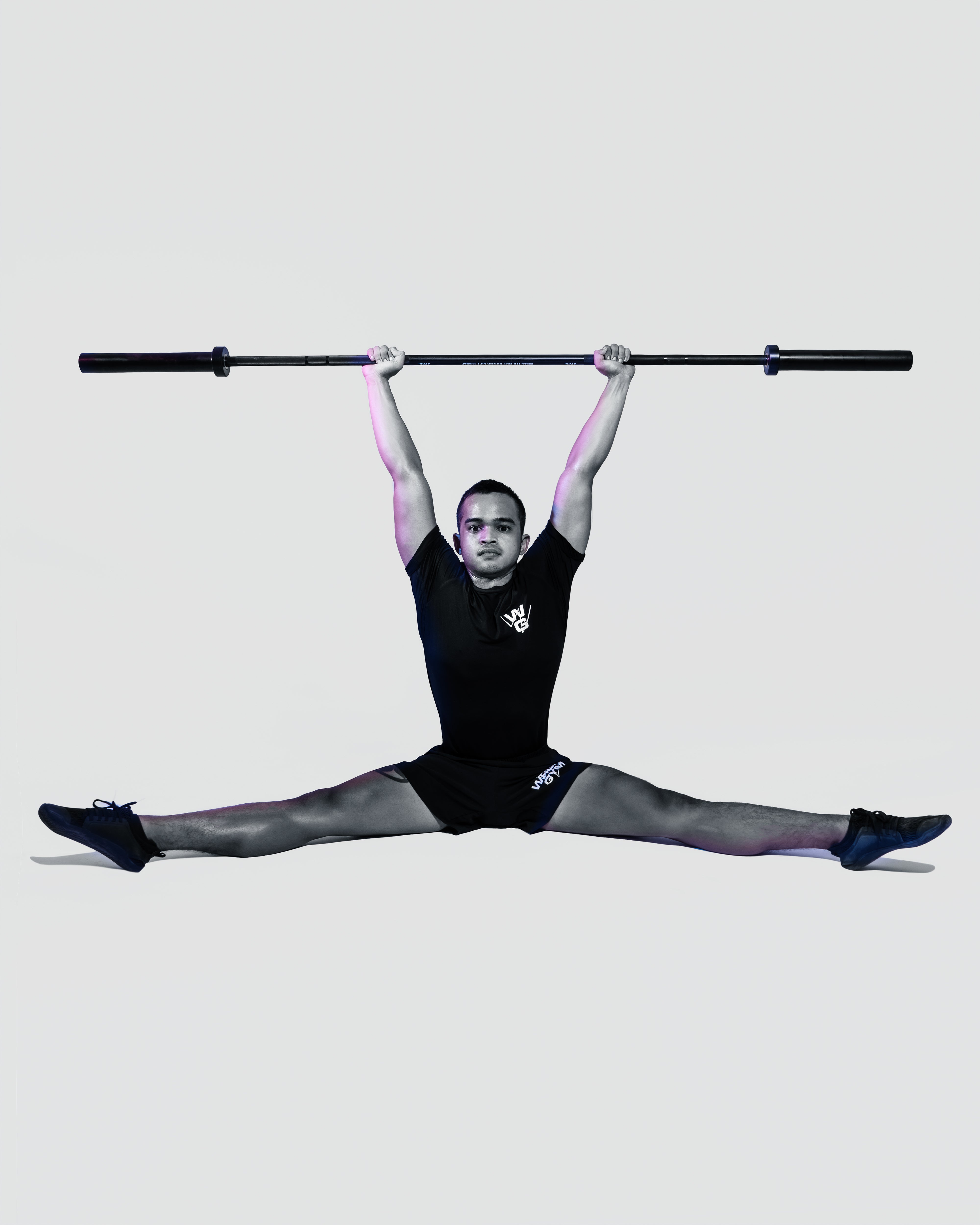 A man performing a split while holding a barbell overhead.